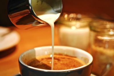 Close-up of milk pouring in coffee on table
