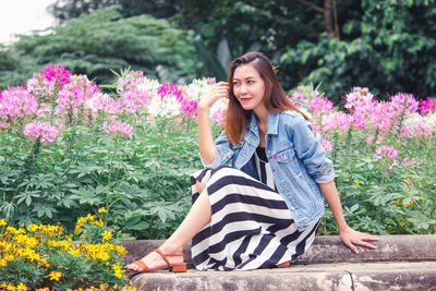 Smiling woman looking away while sitting by pink flowering plants