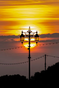 Low angle view of silhouette street lights against orange sky