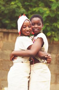 Portrait of female friends in traditional clothing embracing while standing against wall