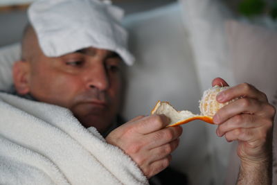 Close-up of man having orange while lying on sofa