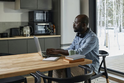 Businessman using laptop on dining table sitting on chair in kitchen at home