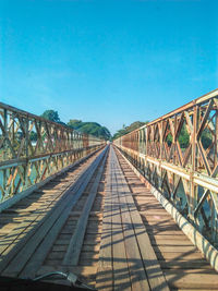 Surface level of footbridge against clear blue sky