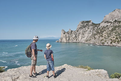 A boy and his grandfather standing on the shore of the bay and looking at the rock. 