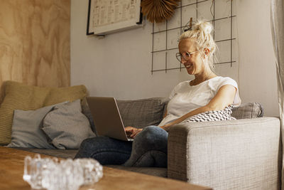 Smiling woman using laptop on sofa