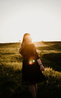 Rear view of woman standing on field against sky during sunset