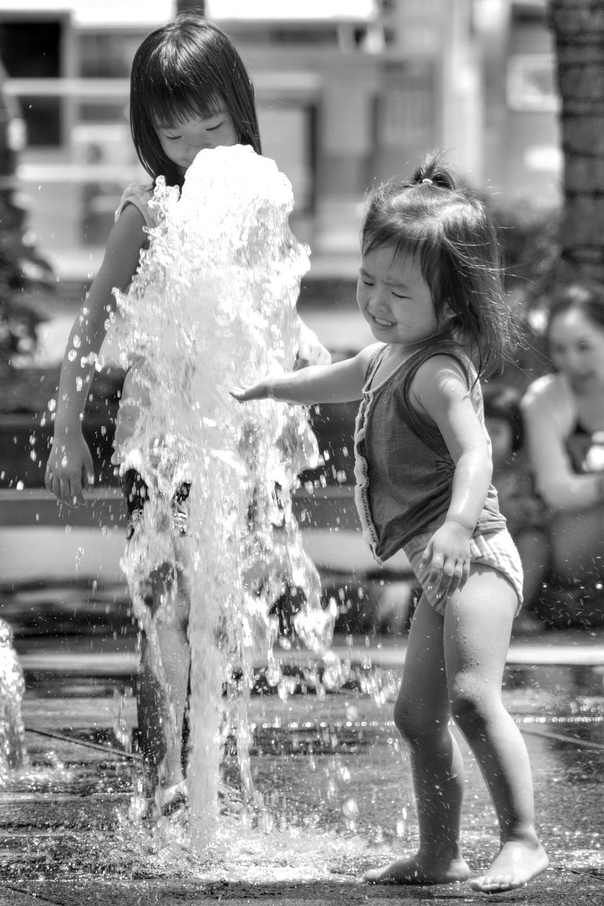 water, lifestyles, childhood, leisure activity, focus on foreground, elementary age, girls, motion, boys, wet, holding, person, splashing, casual clothing, fountain, full length, enjoyment