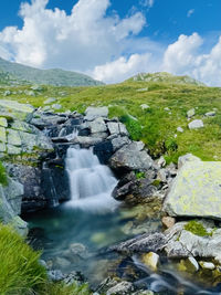 Stream flowing through rocks against sky