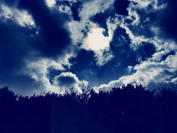 Low angle view of trees against cloudy sky