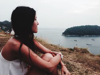 Beautiful woman sitting on cliff by sea against sky