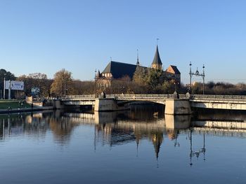 Bridge over river by buildings against clear sky