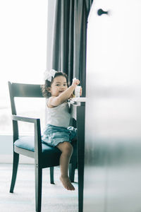 Cute boy looking away while sitting on chair at home