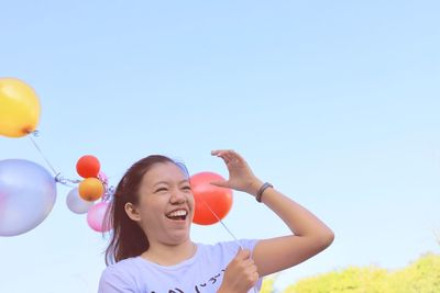 Low angle view of happy girl with balloons against sky