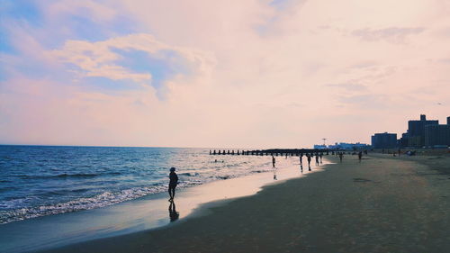 Man walking on beach against sky during sunset