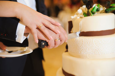 Cropped image of bride and groom cutting wedding cake