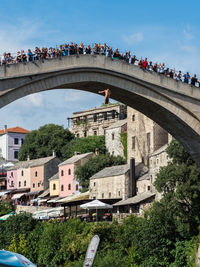 People on bridge by city against sky