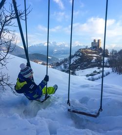 High angle view of boy sitting on swing over snow covered landscape