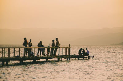 Silhouette people on shore against sky during sunset