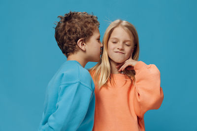Boy whispering in sisters ear against blue background