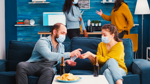 Man giving sanitizer to woman while sitting on sofa at home