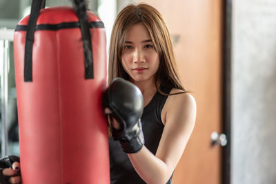 Portrait of confident young woman holding punching bag while standing in gym