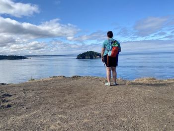 Rear view of man standing on beach against sky