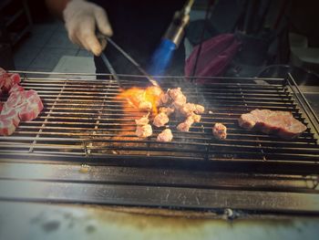 Cropped hands of man cutting meat on barbecue grill