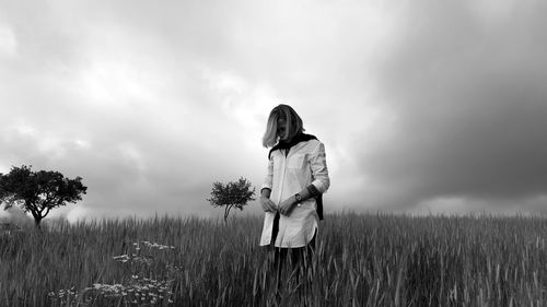 Woman standing on field against cloudy sky