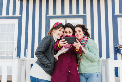 Happy women friends using mobile phone in front of colorful houses.costa nova, aveiro, portugal