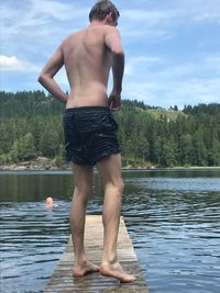 Rear view of shirtless man standing in lake against sky