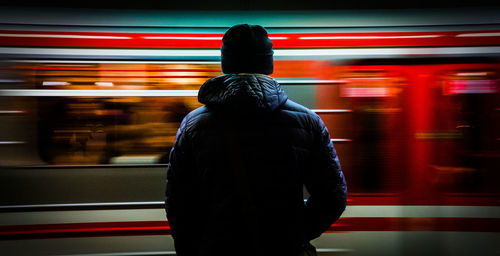 Rear view of man standing against blurred motion of train at railroad station