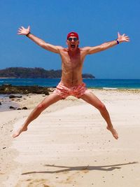 Full length of shirtless man jumping at beach against sky
