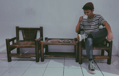 Full length of young man sitting on chair against wall