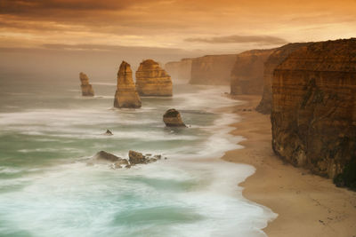 Rocks in sea against sky during sunset