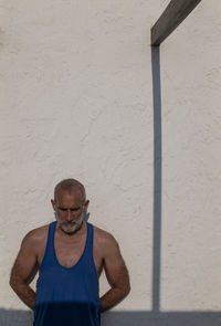 Portrait of adult man against white wall with shadow in summer