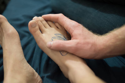 Cropped hand of man touching girlfriend leg on bed