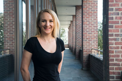 Portrait of smiling young woman standing against brick wall