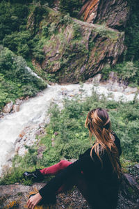 Rear view of woman on rock by river in forest