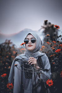 Young woman wearing sunglasses while standing against sky