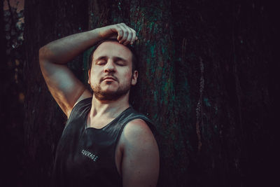 Portrait of young man standing against tree trunk in forest