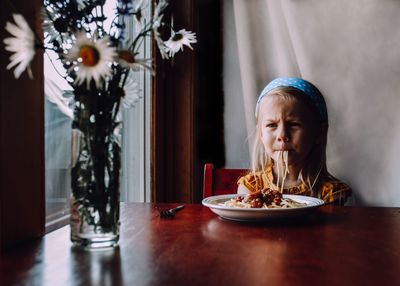 Girl looking away while eating food on table