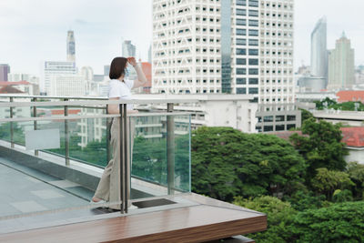 Solo asian woman wear protective mask during outdoor break and relax at rooftop with city background