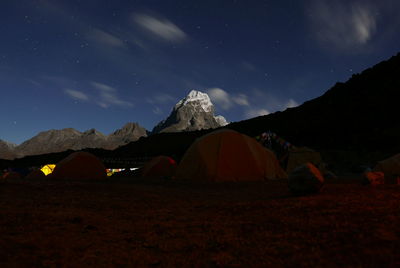 Tents by rocky mountains against sky at night