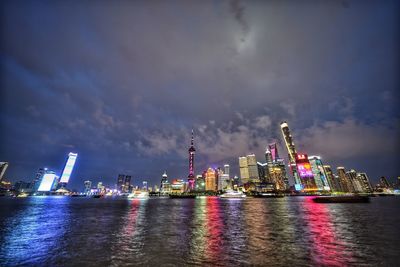 Illuminated buildings by sea against sky