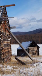 Log houses on snow covered field against cloudy sky during winter