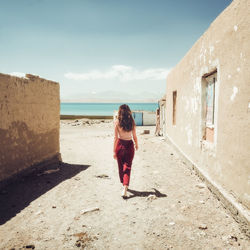 Rear view of woman walking by sea against buildings