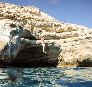 Man jumping on rock by sea against clear sky