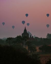 Silhouette hot air balloons flying over temple against sky during sunset