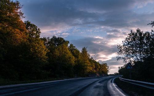 Road by trees against sky during sunset