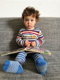 Portrait of cute boy with book sitting on sofa at home